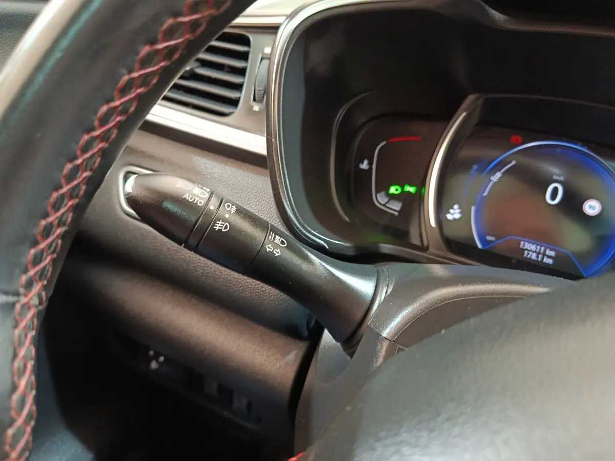 Gros plan sur la manette de phares et clignotants à gauche du volant cuir du Renault Kadjar blanc, tableau de bord digital visible.