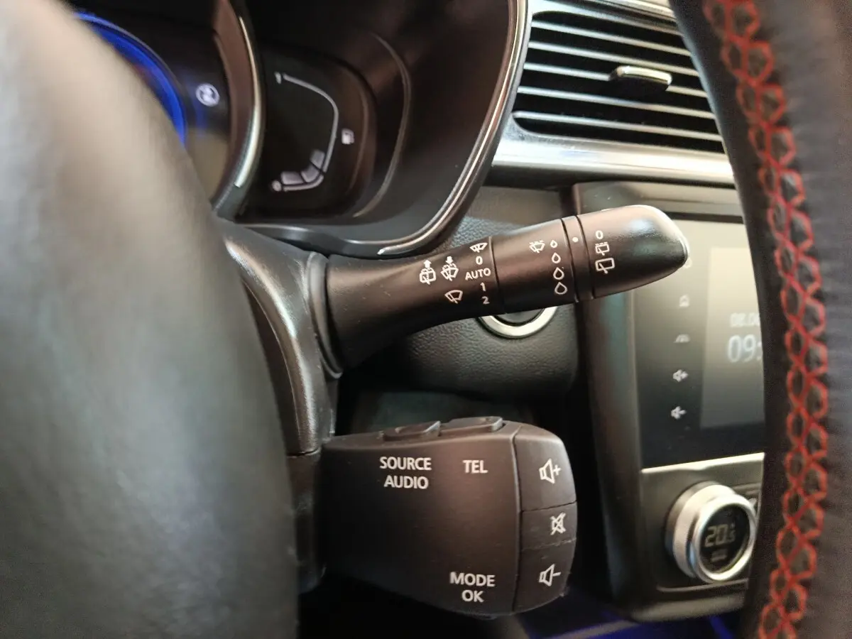 Gros plan intérieur sur commandes au volant du Renault Kadjar blanc, avec volant cuir noir et surpiqûres rouges visibles.