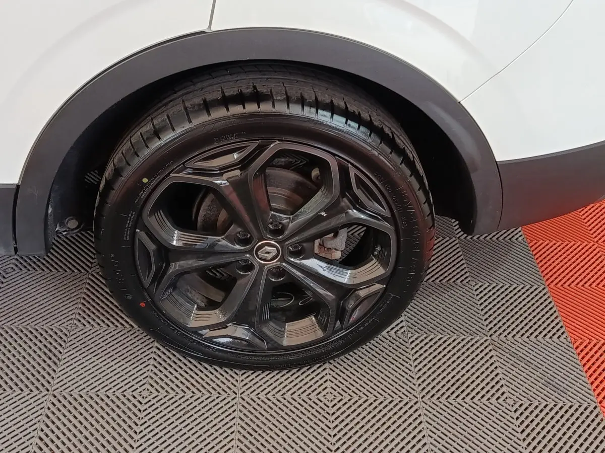 Gros plan sur la roue arrière droite noire brillante d’un Renault Kadjar blanc, avec logo Renault au centre.