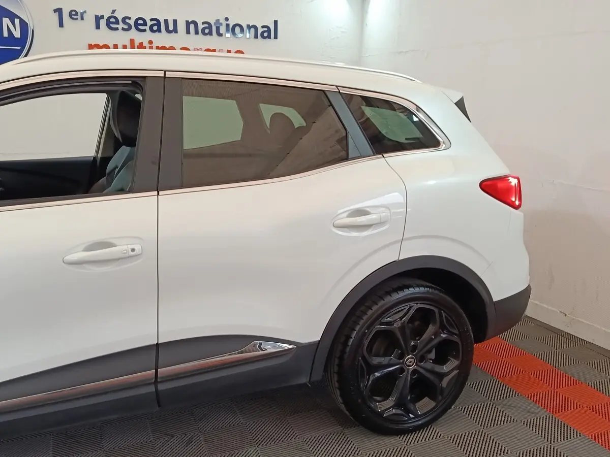 Vue de profil côté droit sur la partie arrière d'un Renault Kadjar blanc avec jantes noires et feux arrière allumés.