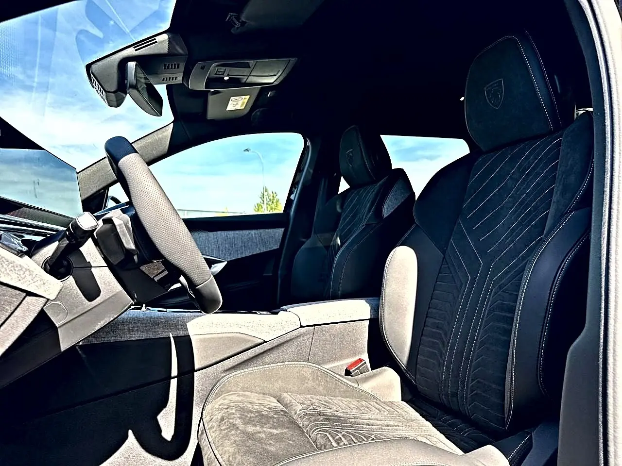 Vue intérieure côté conducteur du Peugeot 5008 Hybrid 145 GT e-dcs6 2025 avec sièges noirs en alcantara et logo Peugeot brodé.