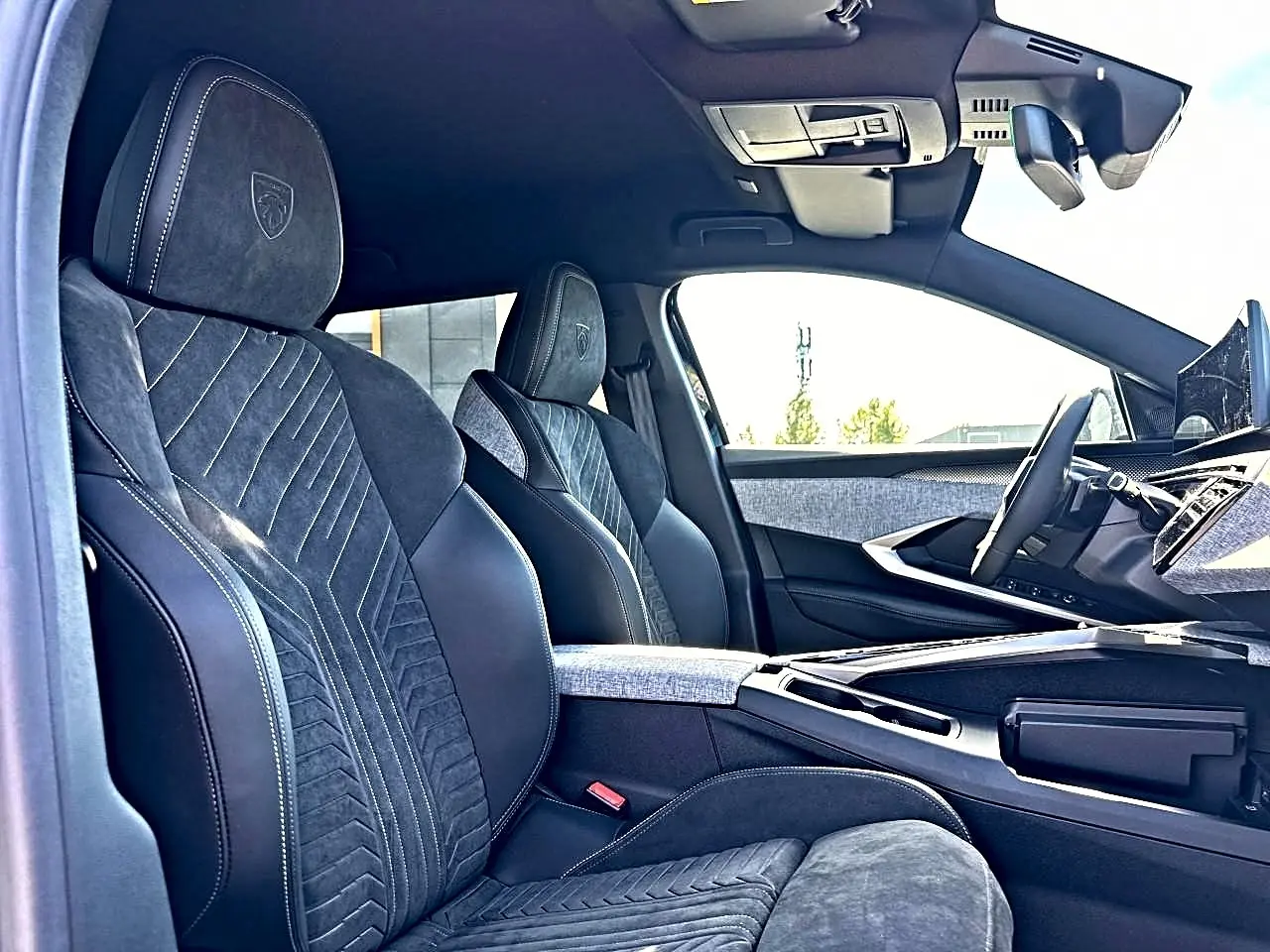 Vue intérieure côté conducteur du Peugeot 5008 Hybrid 145 GT e-dcs6 2025, sièges noirs en cuir et alcantara avec surpiqûres blanches.