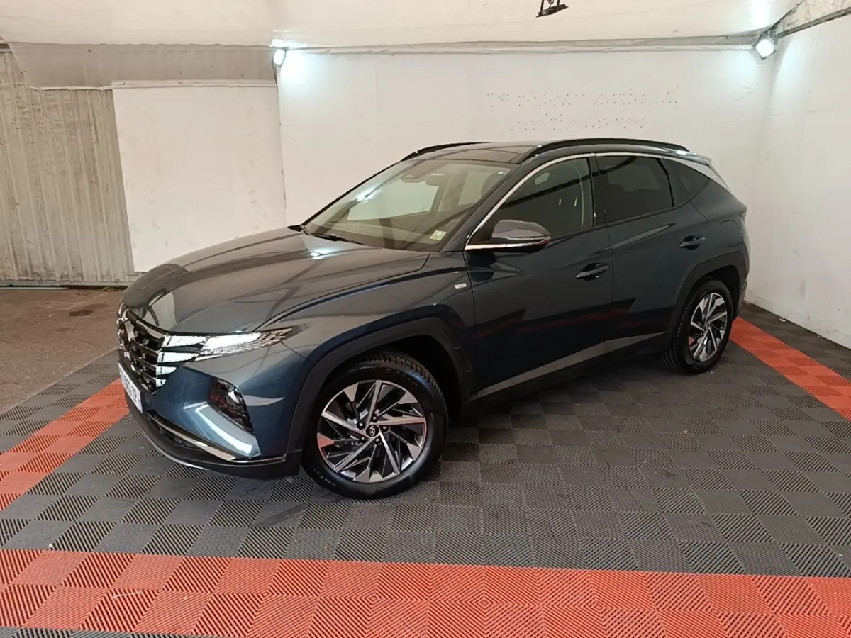 Vue 3/4 avant droit du Hyundai Tucson bleu métallisé avec jantes alliage et toit noir dans un garage.