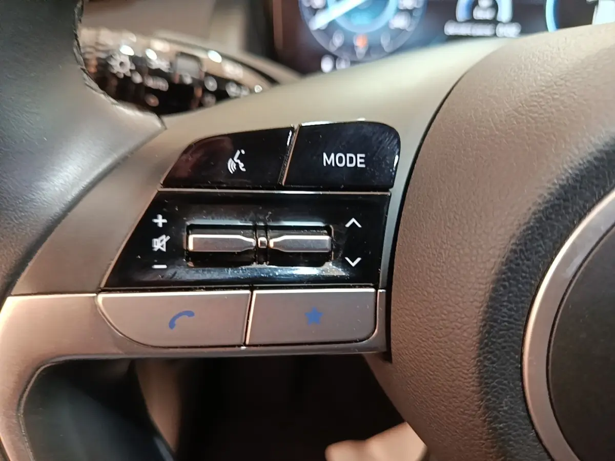 Gros plan sur les commandes gauche du volant gris du Hyundai Tucson bleu 2021, avec boutons mode et téléphone.