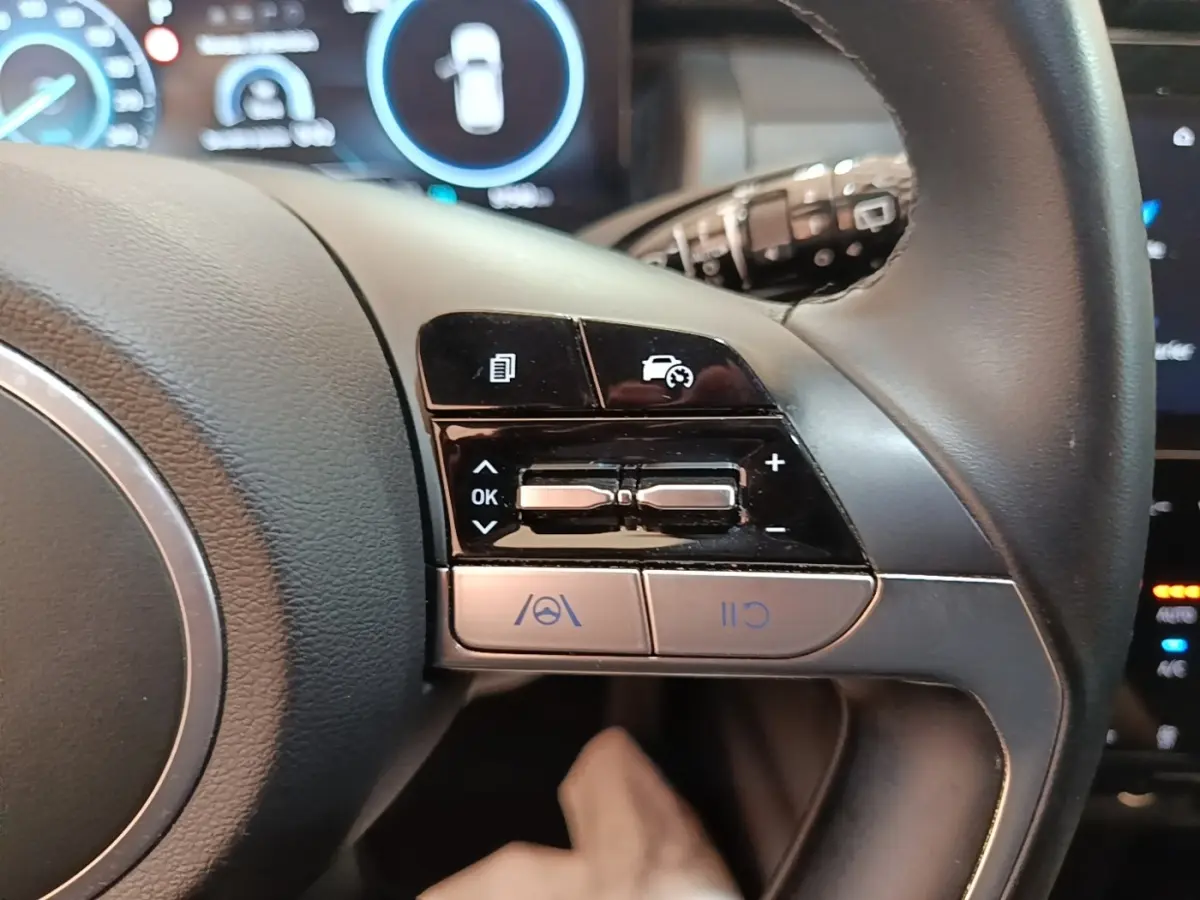 Gros plan sur les commandes du volant cuir et alu du Hyundai Tucson bleu 2021, avec affichage digital en arrière-plan.