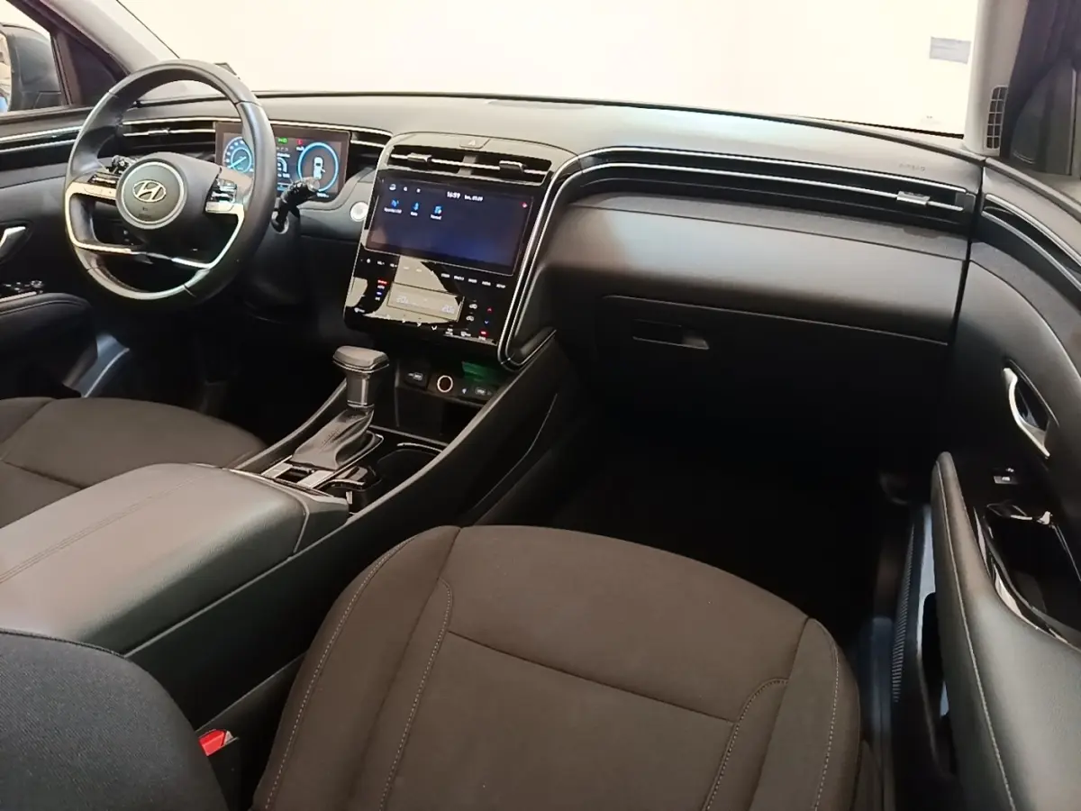 Vue intérieure avant droite du Hyundai Tucson 2021, tableau de bord noir avec écran tactile central et volant multifonctions.