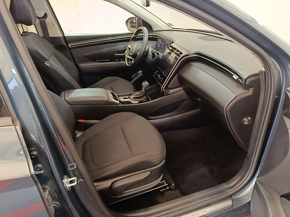 Vue intérieure côté conducteur du Hyundai Tucson bleu 2021, montrant sièges noirs et tableau de bord digital.