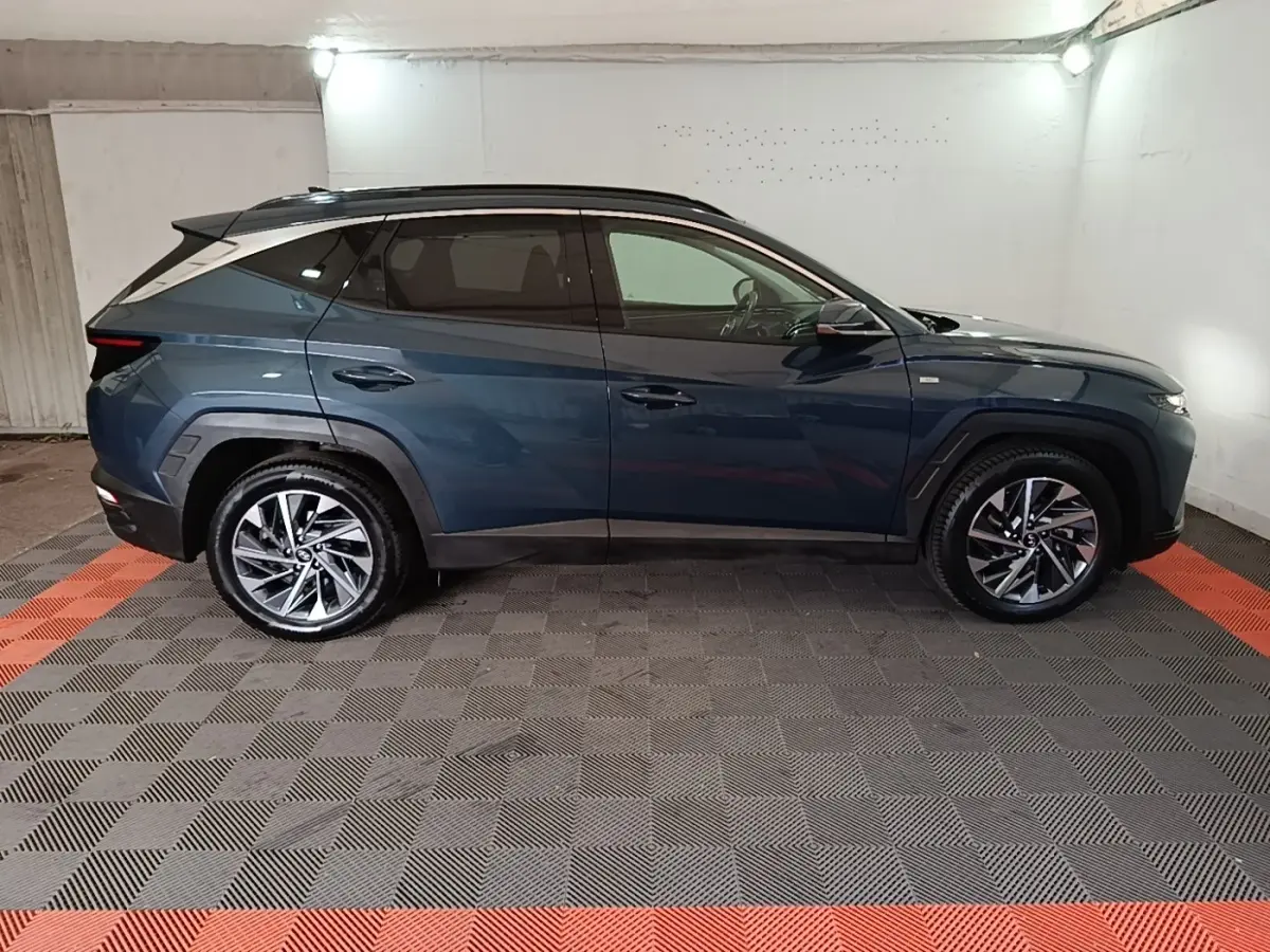 Vue de profil côté gauche d’un Hyundai Tucson bleu 2021 avec jantes alliage et toit noir dans un garage.