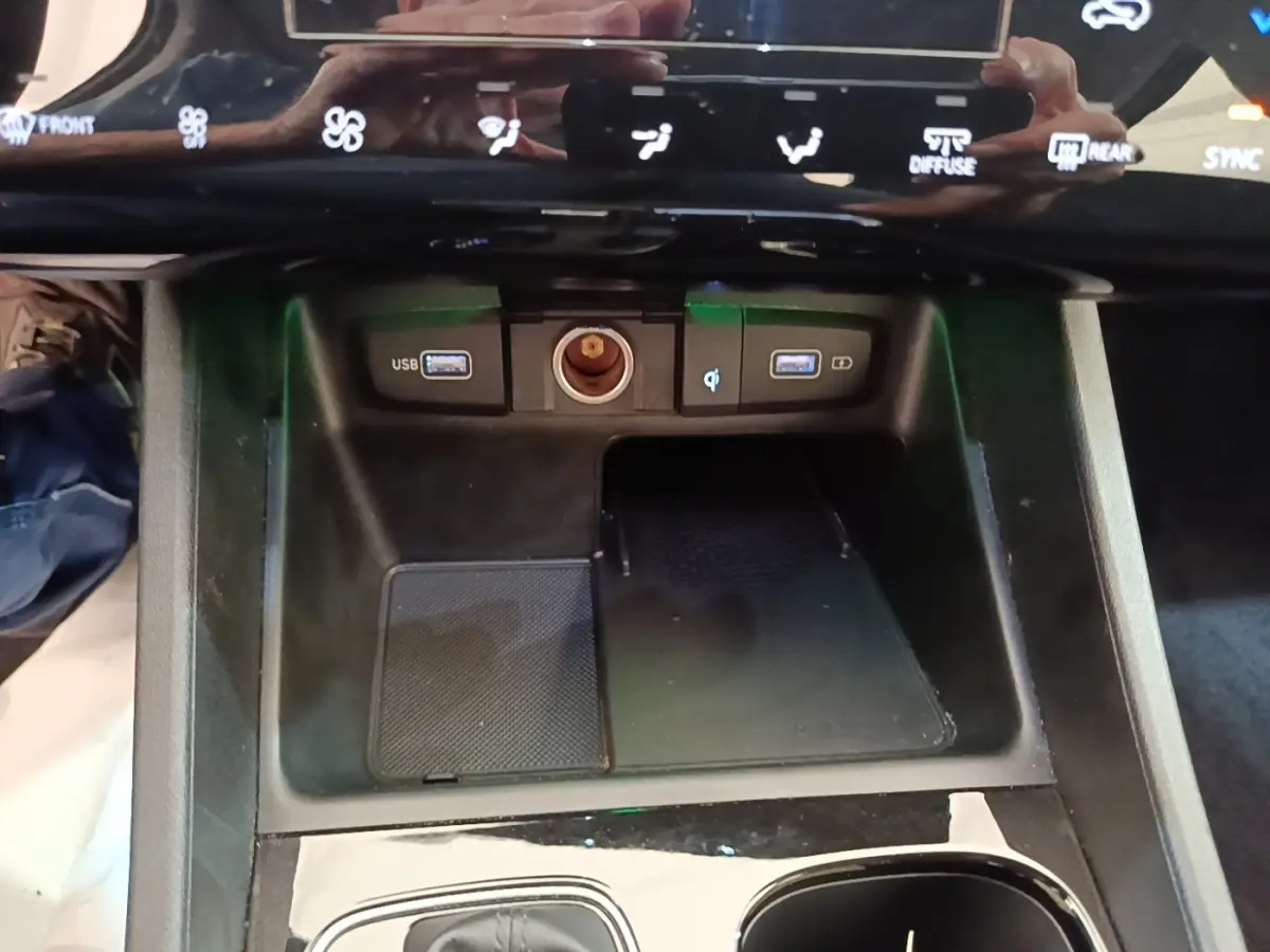 Gros plan sur la console centrale noire du Hyundai Tucson hybride 2021 avec ports USB, prise 12V et zone de recharge sans fil.
