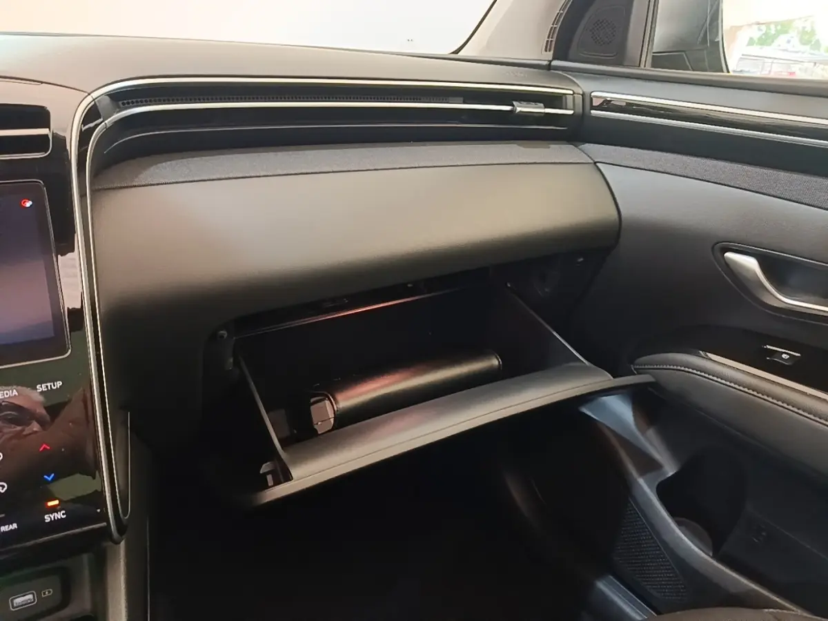 Intérieur du Hyundai Tucson bleu 2021, vue côté passager avec boîte à gants ouverte et tableau de bord noir.