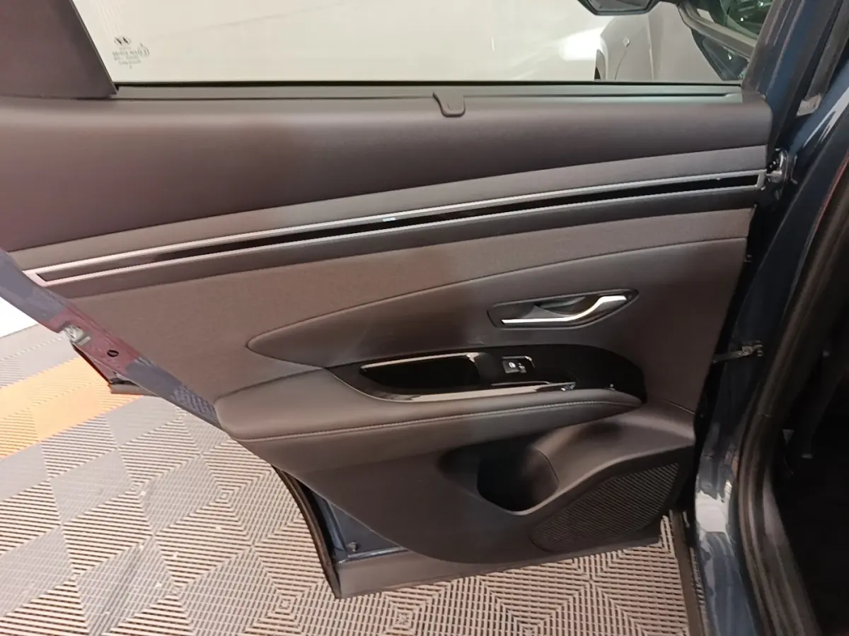 Vue intérieure de la porte arrière droite du Hyundai Tucson bleu, avec garniture noire et commandes de fenêtre.
