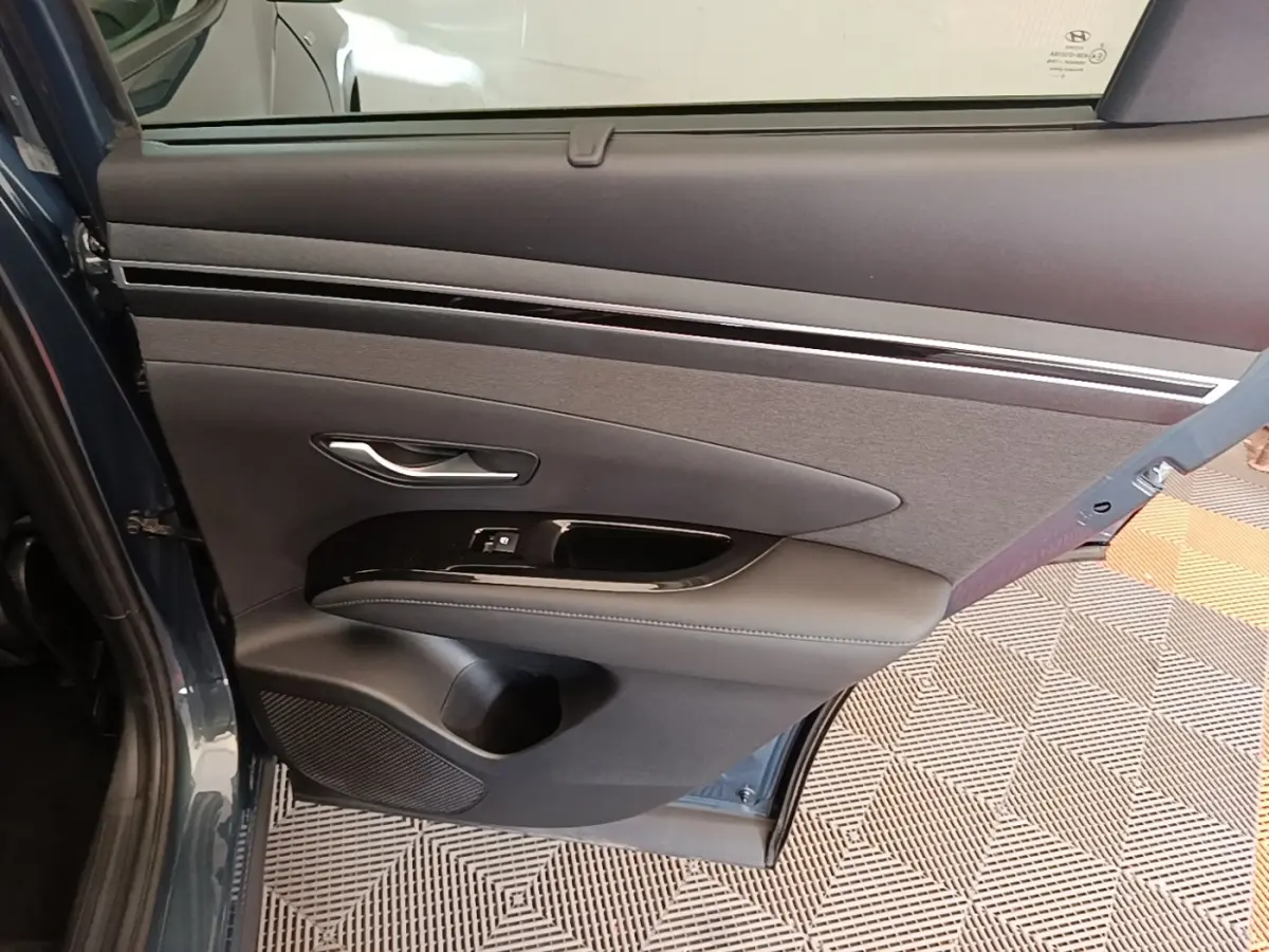 Vue intérieure de la porte arrière gauche bleu foncé du Hyundai Tucson 2021 avec garniture noire et commandes de fenêtre.