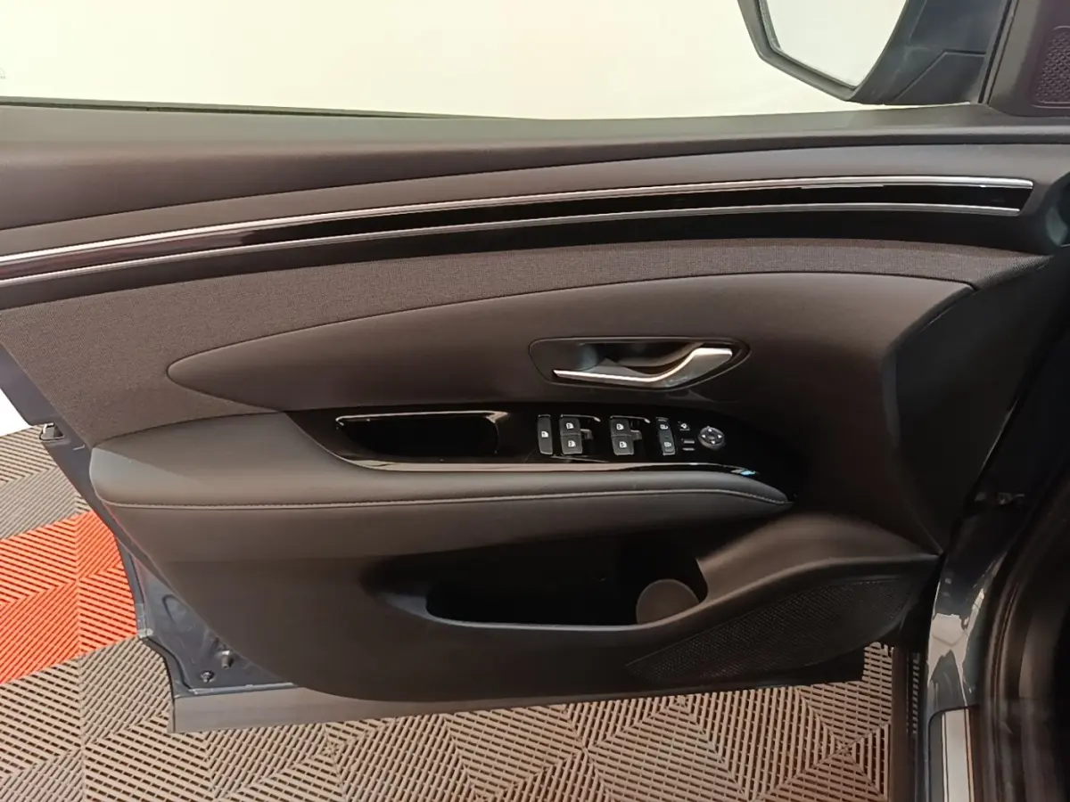 Vue côté gauche de la porte avant d’un Hyundai Tucson bleu, avec commandes de vitres et poignée argentée.