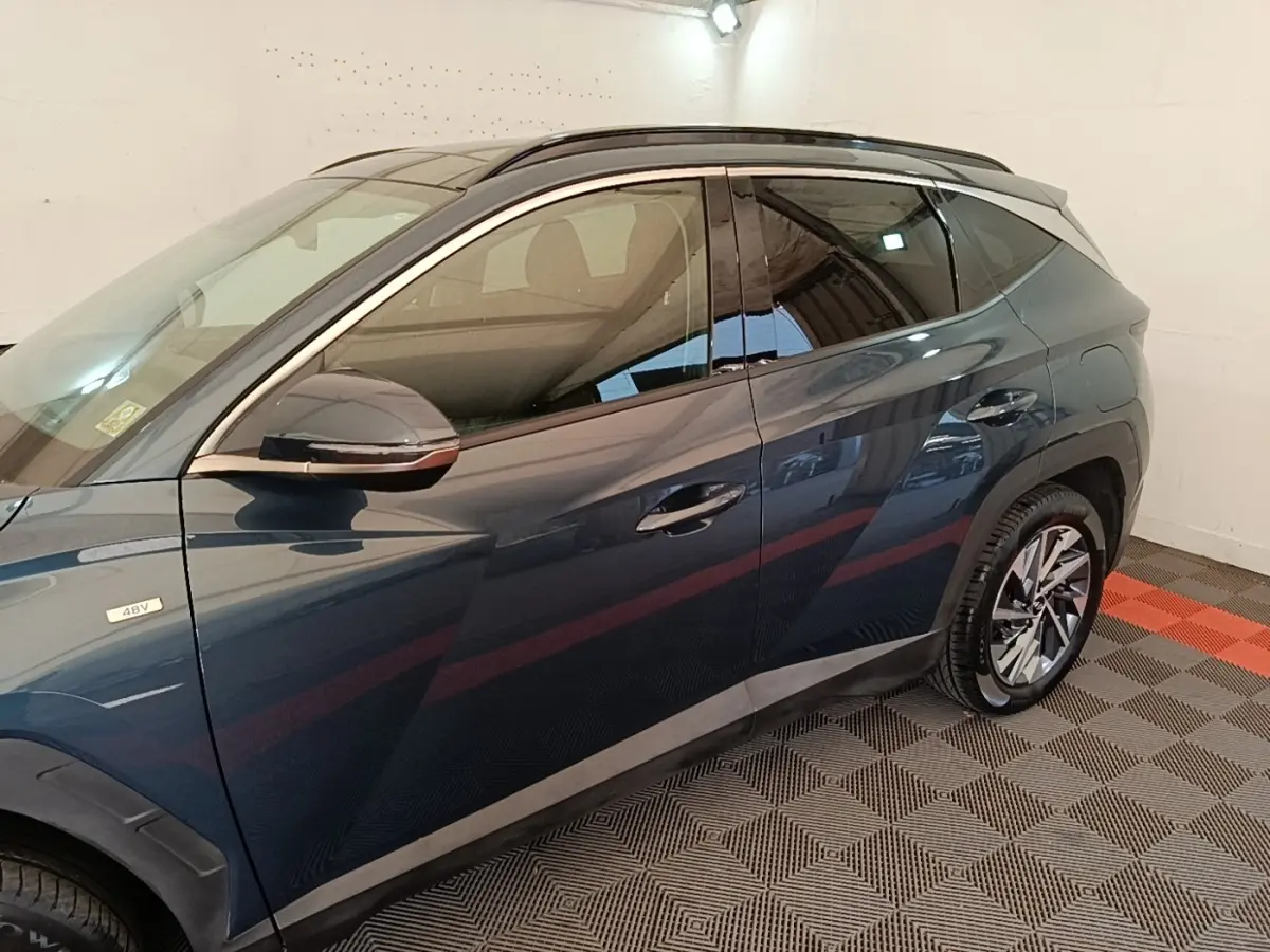 Vue côté gauche du Hyundai Tucson bleu hybride 48V, mettant en valeur les jantes alliage et le rétroviseur chromé.