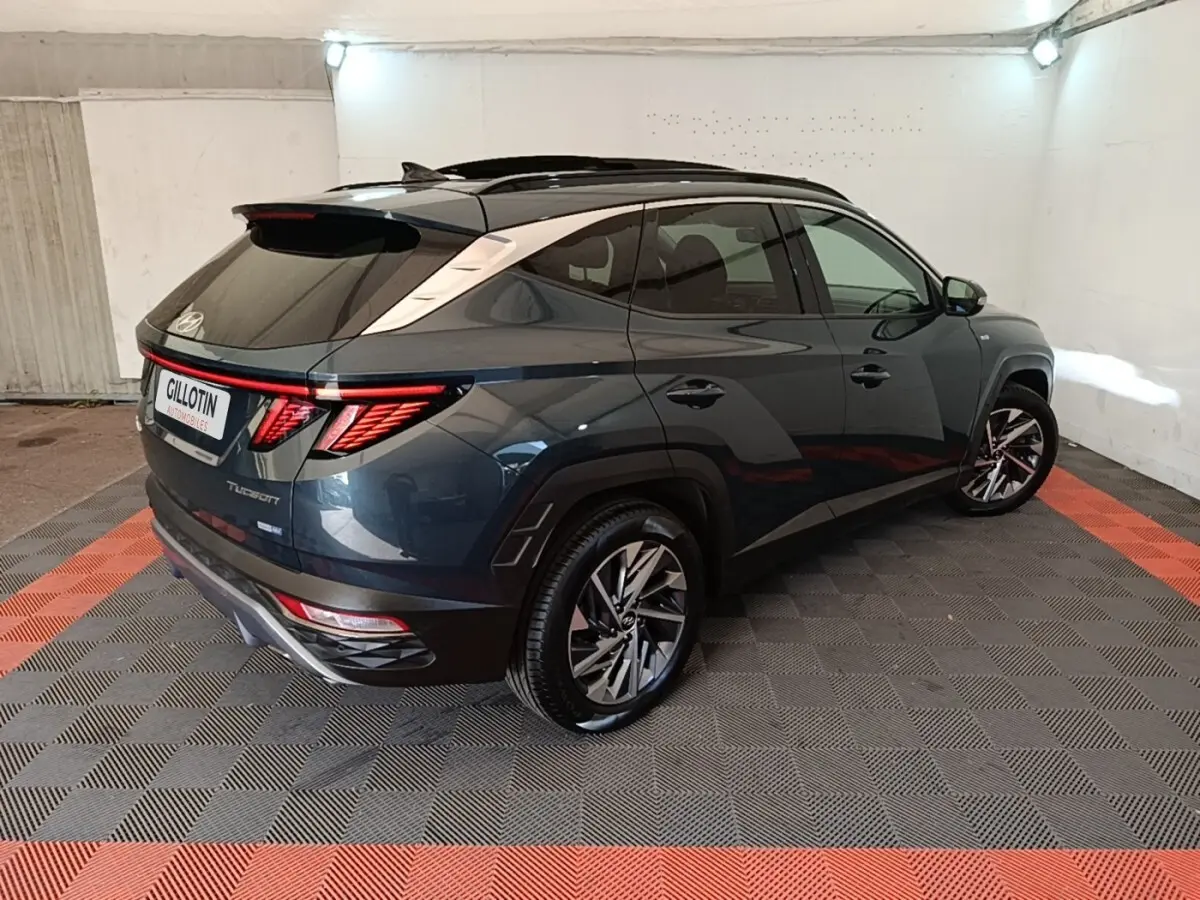 Vue 3/4 arrière droite d’un Hyundai Tucson bleu foncé avec toit noir et feux arrière LED distinctifs dans un garage.