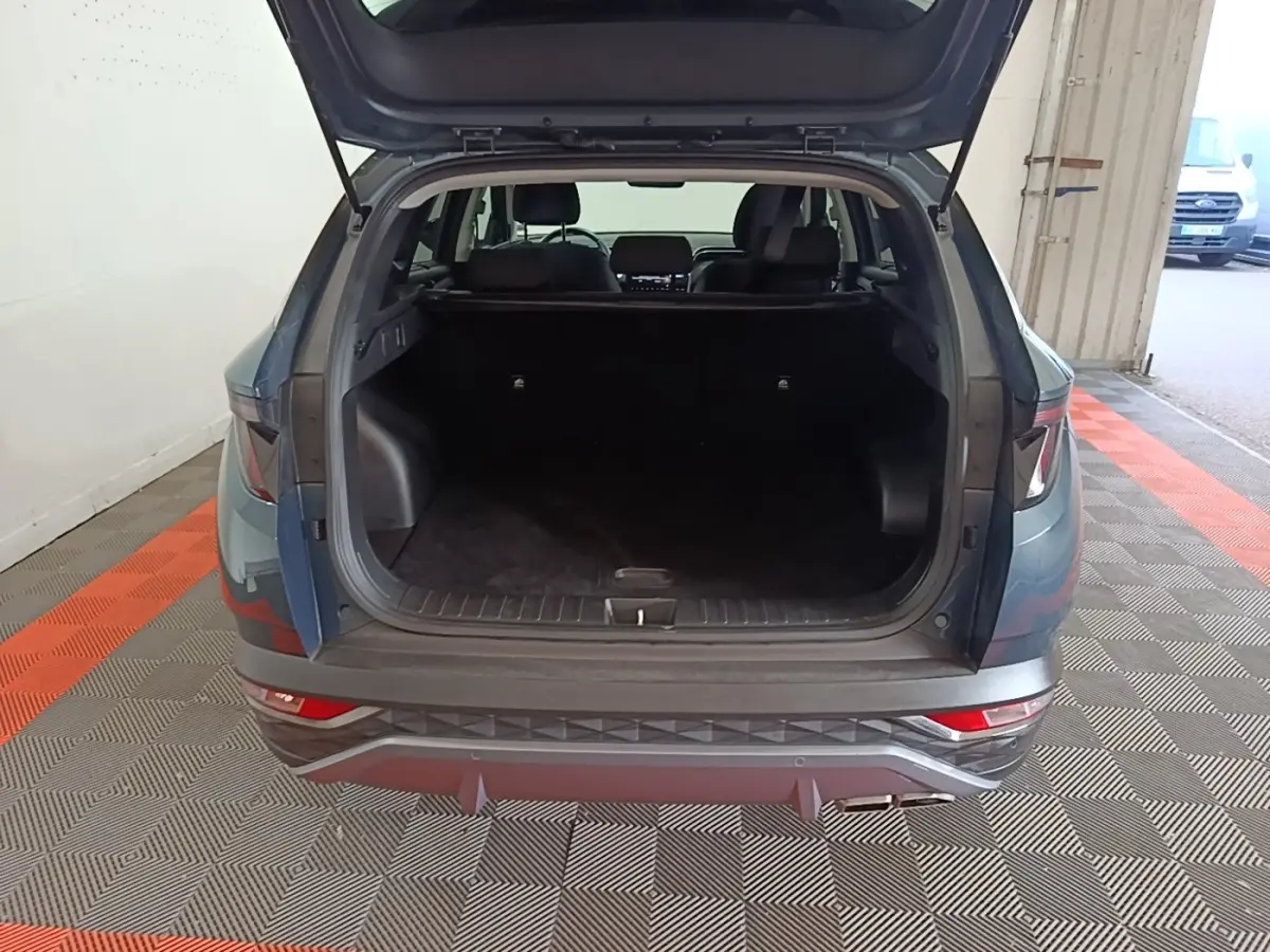 Vue arrière du Hyundai Tucson bleu 2021 avec coffre ouvert montrant un espace de chargement spacieux et intérieur sombre.