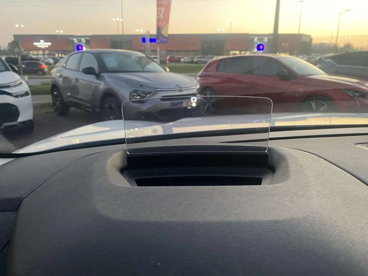 Vue depuis l'habitacle montrant le pare-brise et l'affichage tête haute d'une Citroën C4 blanche stationnée en extérieur au crépuscule.