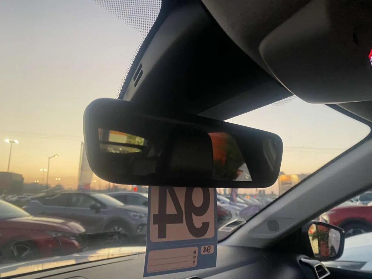 Vue intérieure centrée sur le rétroviseur intérieur d'une Citroën C4 blanche, avec parking en arrière-plan au crépuscule.