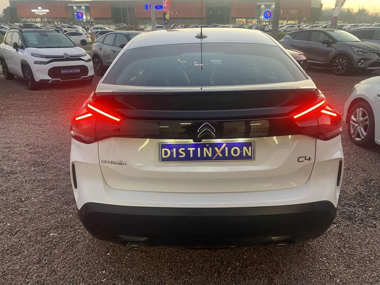 Vue arrière d'une Citroën C4 blanche de 2021 avec feux arrière allumés et plaque Distinxion visible.