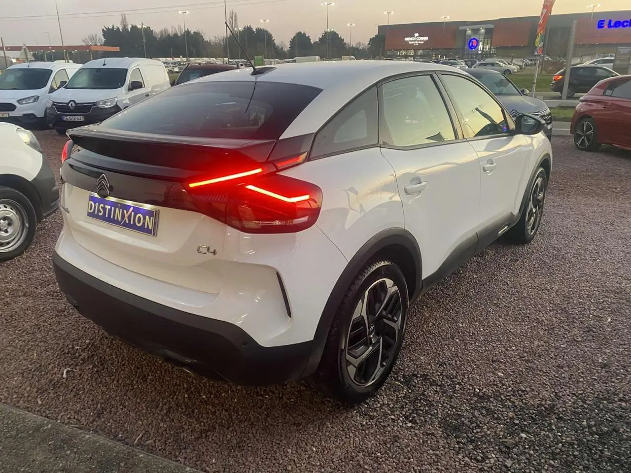 Vue 3/4 arrière droite d'une Citroën C4 blanche avec feux arrière LED allumés sur parking extérieur.