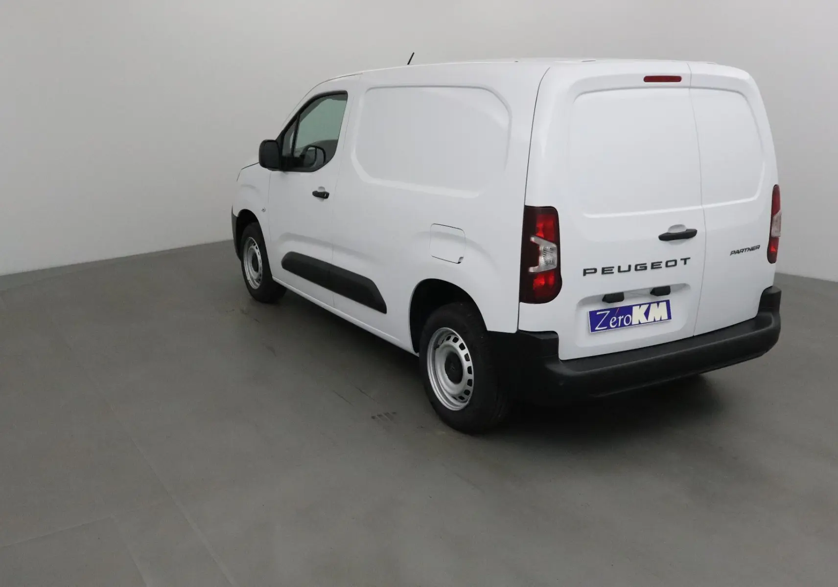 Peugeot Partner blanc vue 3/4 arrière droit, fourgon utilitaire avec portes arrière pleines et pare-chocs noirs.