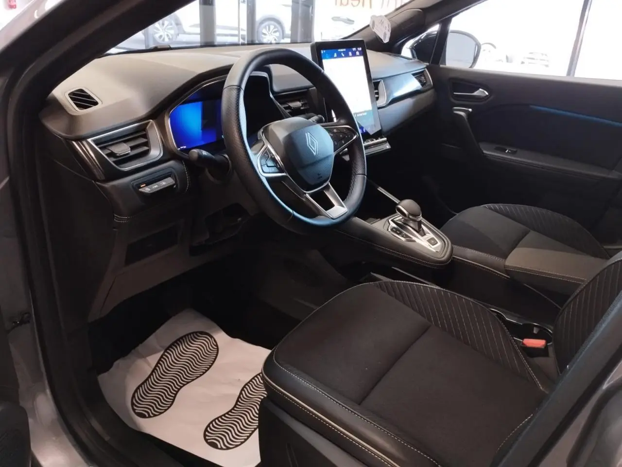 Vue intérieure côté conducteur du Renault Symbioz 2025, montrant le volant, écran tactile vertical et sièges noirs.