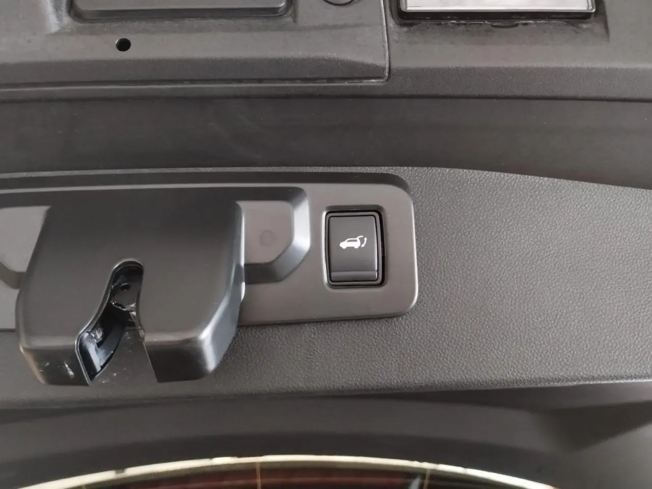 Bouton d'ouverture électrique du hayon sur la partie intérieure d'un Renault Symbioz gris Cassiopée, vue en gros plan.