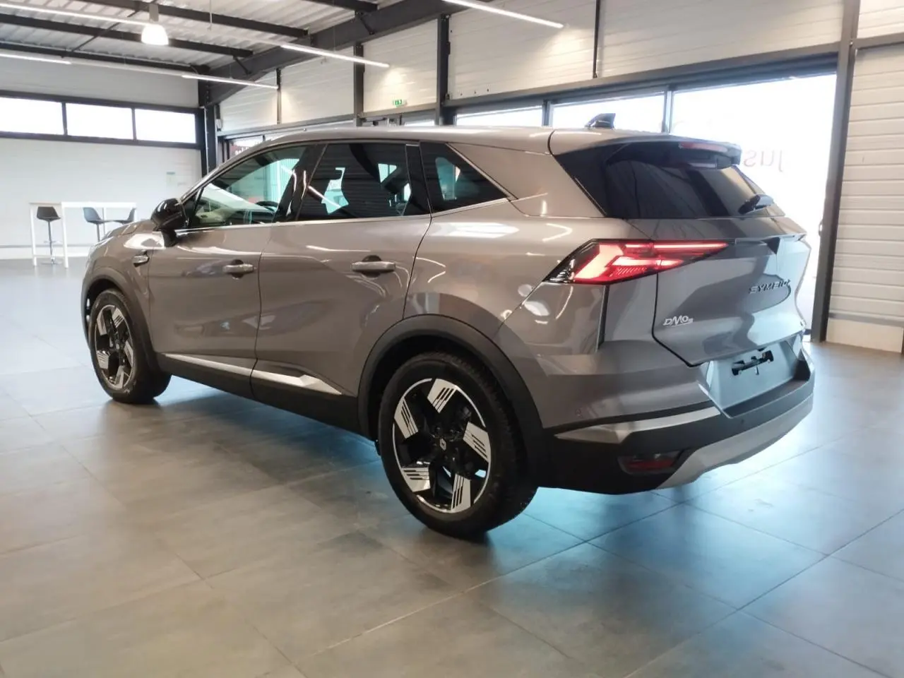 Renault SYMBIOZ gris Cassiopée en vue 3/4 arrière droit, avec jantes 18 pouces et feux arrière LED allumés.