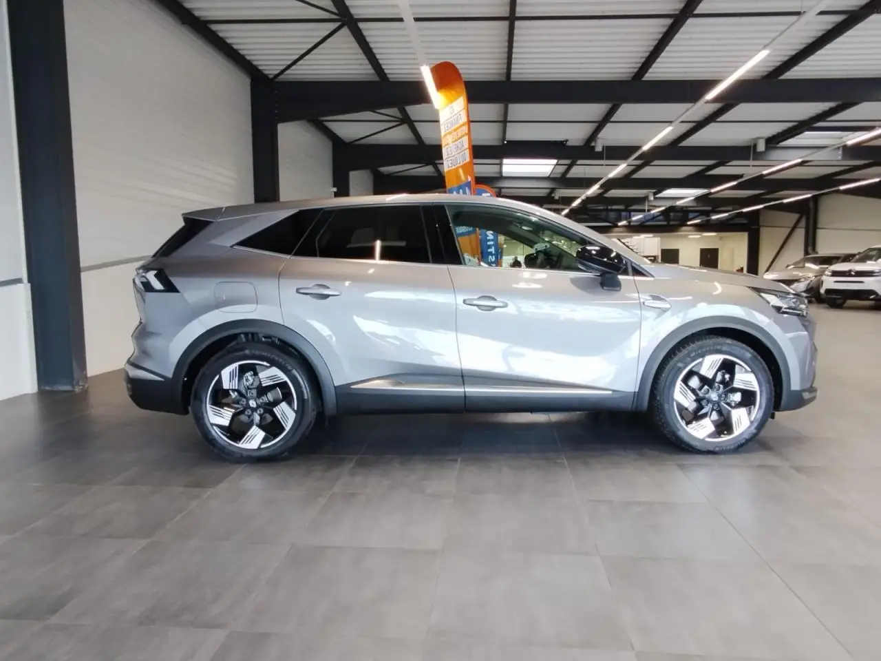Renault Symbioz gris Cassiopée vue de profil côté gauche en intérieur avec jantes alliage distinctives.