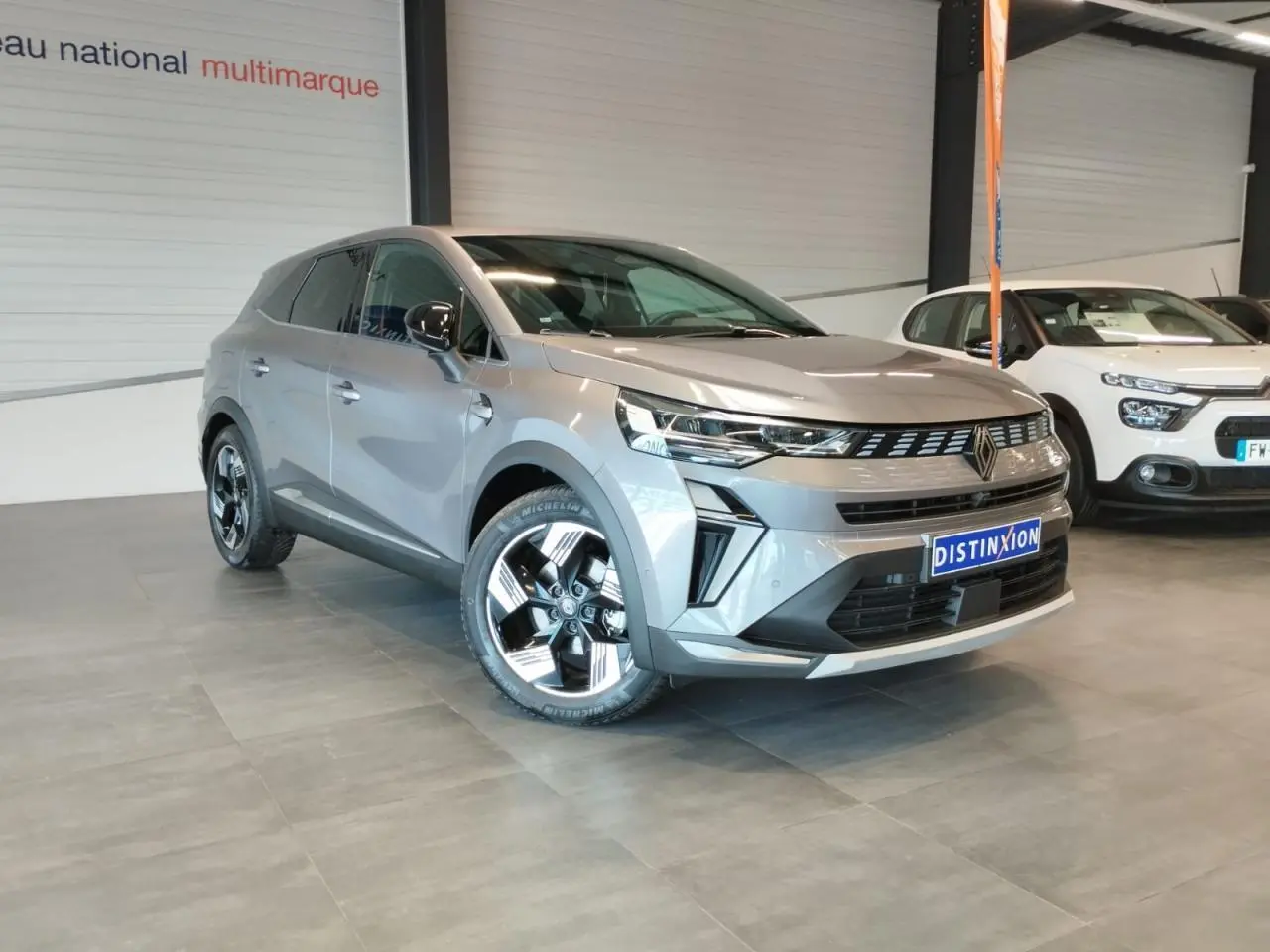 Renault Symbioz gris Cassiopée en 3/4 avant droit, avec jantes alliage 18 pouces et calandre noire distinctive.