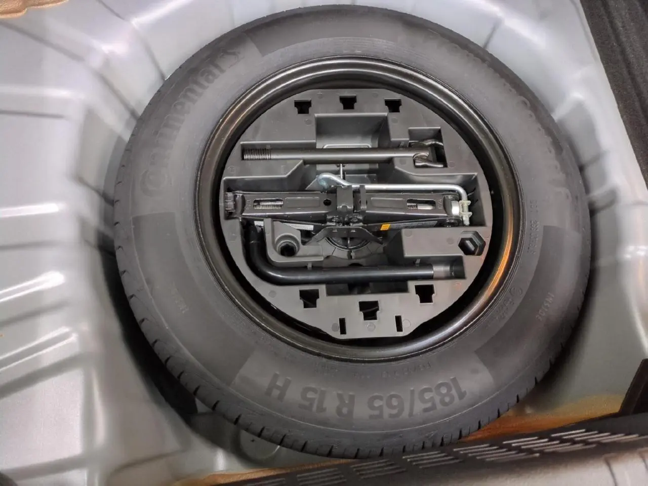 Gros plan sur la roue de secours tôle noire et ses outils dans le coffre d'une Renault Clio gris foncé 2024.