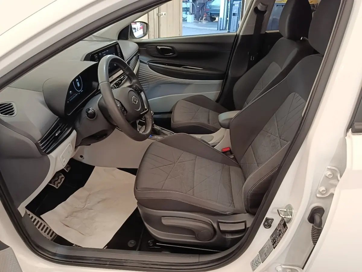 Vue intérieure côté conducteur de la Hyundai Bayon blanche 2024, montrant sièges tissu gris et tableau de bord digital.