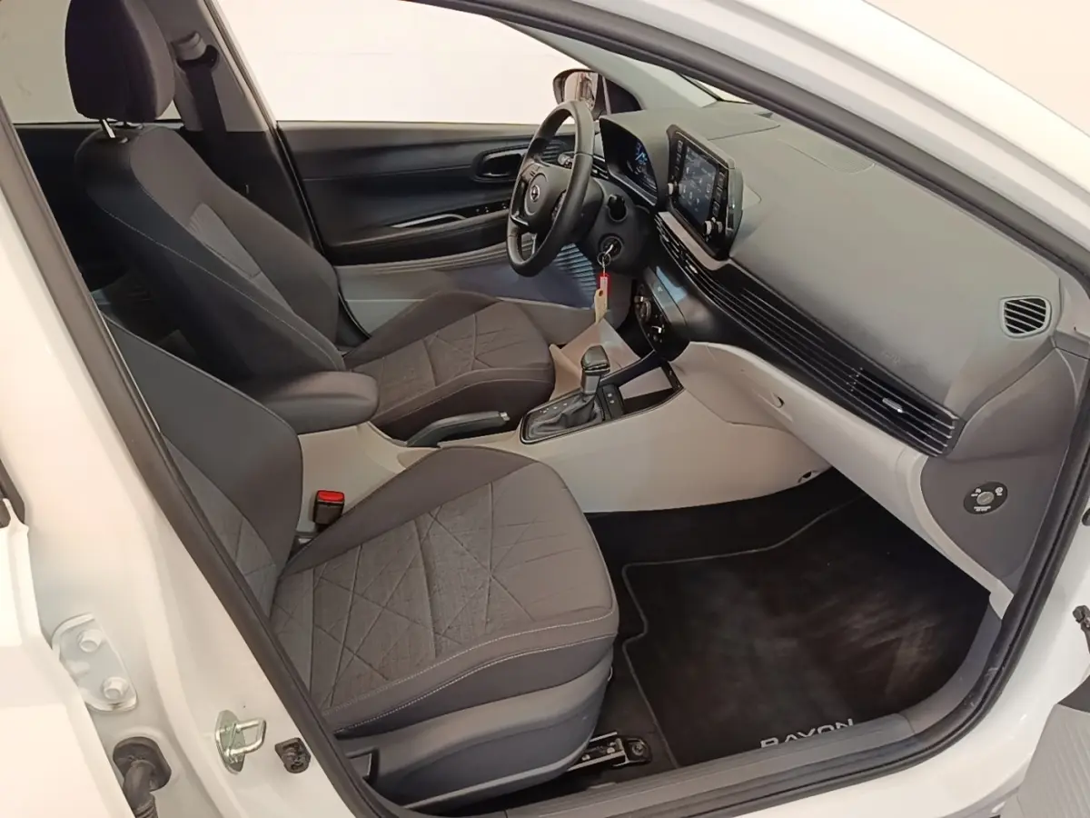 Vue intérieure côté conducteur de la Hyundai Bayon blanche 2024, montrant sièges noirs et tableau de bord moderne avec écran tactile.