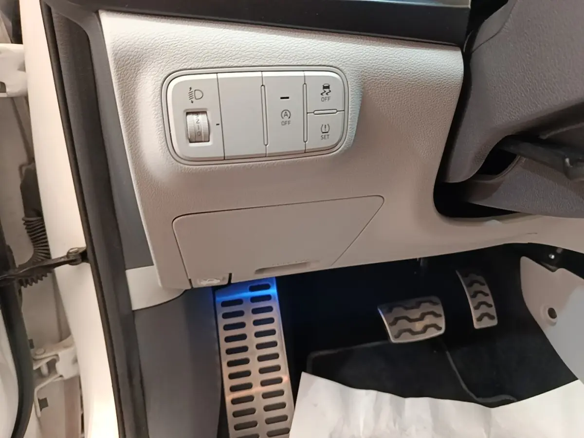 Détail intérieur côté conducteur du Hyundai Bayon blanc 2024, avec commandes d'éclairage et pédales en aluminium.