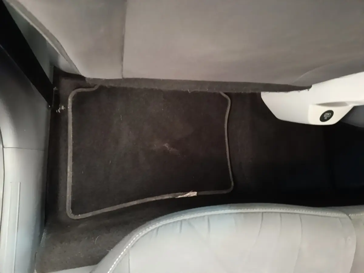 Vue intérieure du sol côté passager avant du Hyundai Bayon 2024 blanc avec tapis de sol noir et partie inférieure de siège visible.
