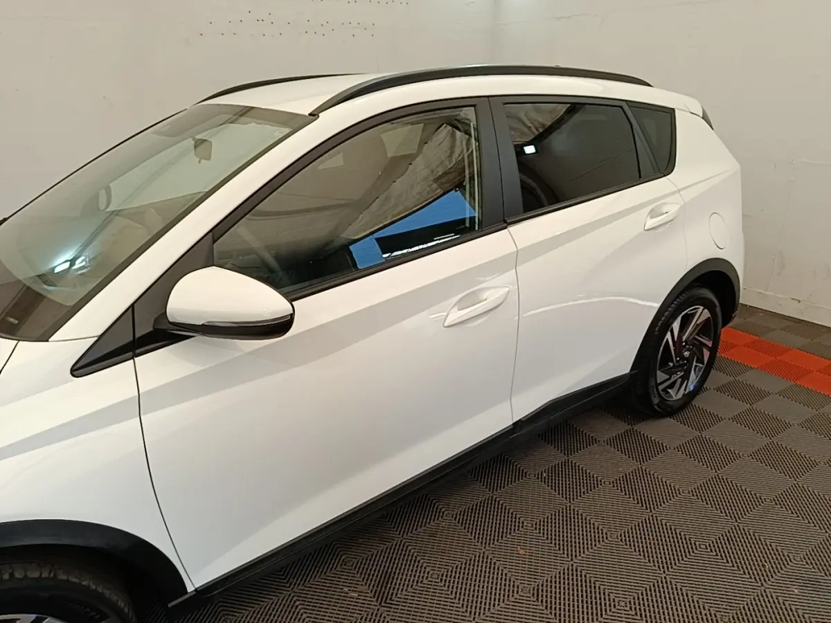 Vue latérale droite d'une Hyundai Bayon blanche 2024 avec jantes alliage et rétroviseurs blancs dans un garage.