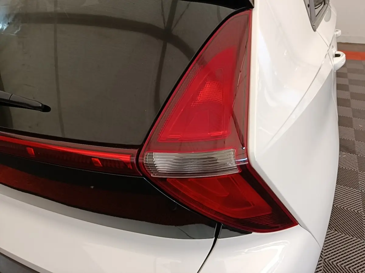 Gros plan sur le feu arrière droit rouge et blanc du Hyundai Bayon blanc, avec partie vitrée noire du coffre visible.