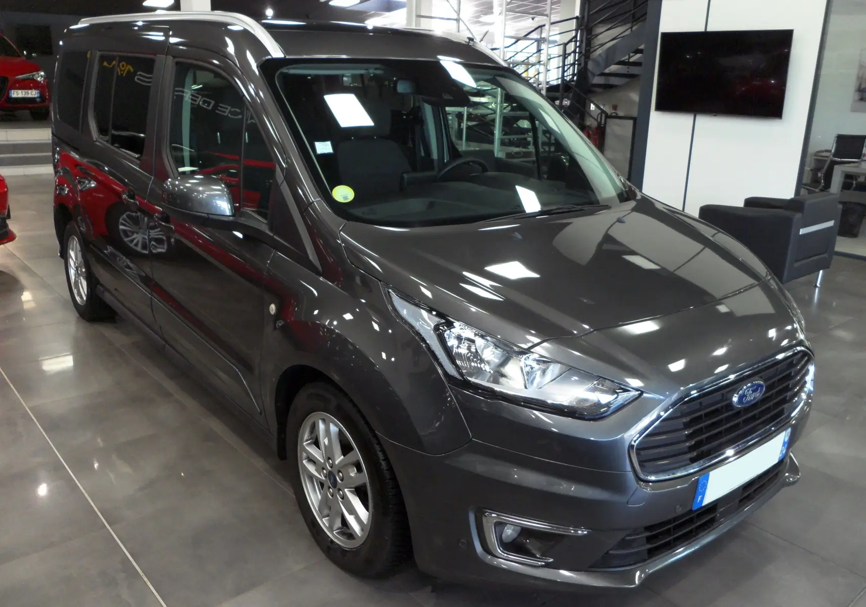 Ford Grand Tourneo Connect gris Magnetic en 3/4 avant droit dans un showroom lumineux avec jantes alliage.
