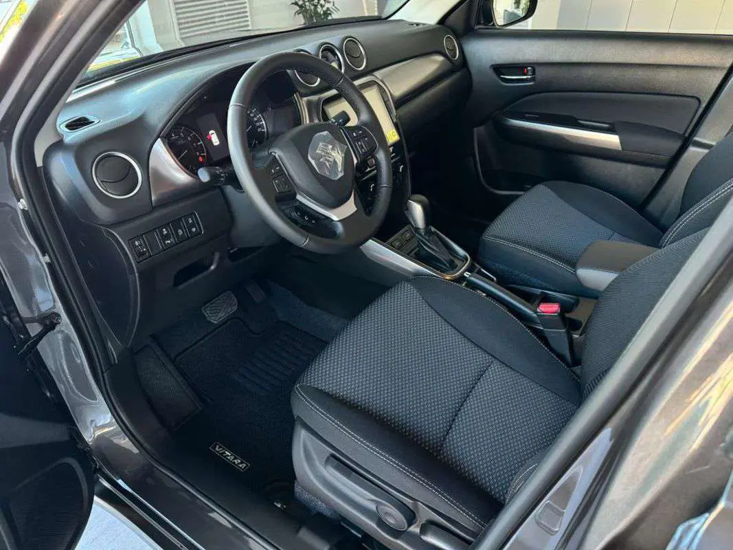 Intérieur côté conducteur du Suzuki Vitara 2025 blanc nacré, montrant le tableau de bord et les sièges noirs tissu.