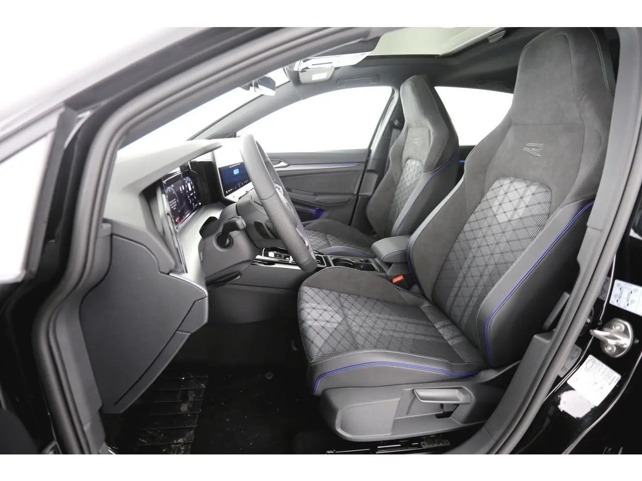Vue intérieure côté conducteur de la Volkswagen Golf VIII R-Line 2026, sièges sport gris avec surpiqûres bleues et volant cuir.