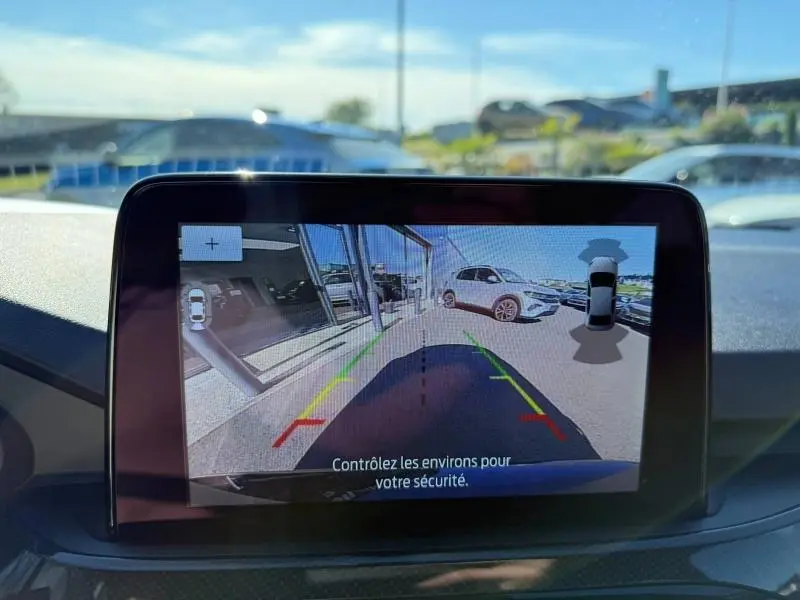 Écran de caméra de recul du Ford Kuga 2024 montrant l'arrière avec lignes de guidage colorées et véhicule blanc à droite.