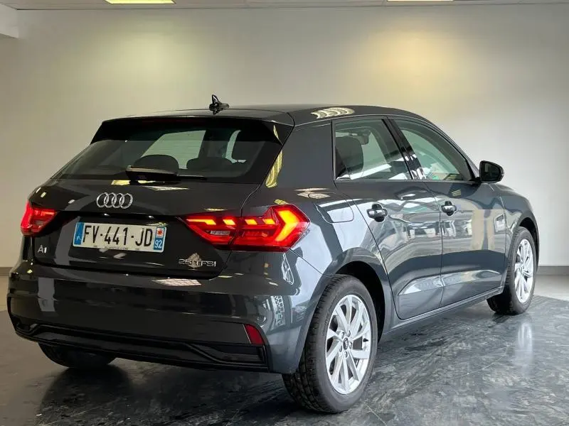 Audi A1 Sportback noir métallisé vue 3/4 arrière droit avec feux arrière LED allumés dans un intérieur neutre.