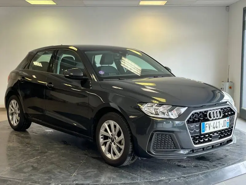 Audi A1 Sportback noir Mythic métallisé vue 3/4 avant droit dans un showroom lumineux avec jantes alu visibles.