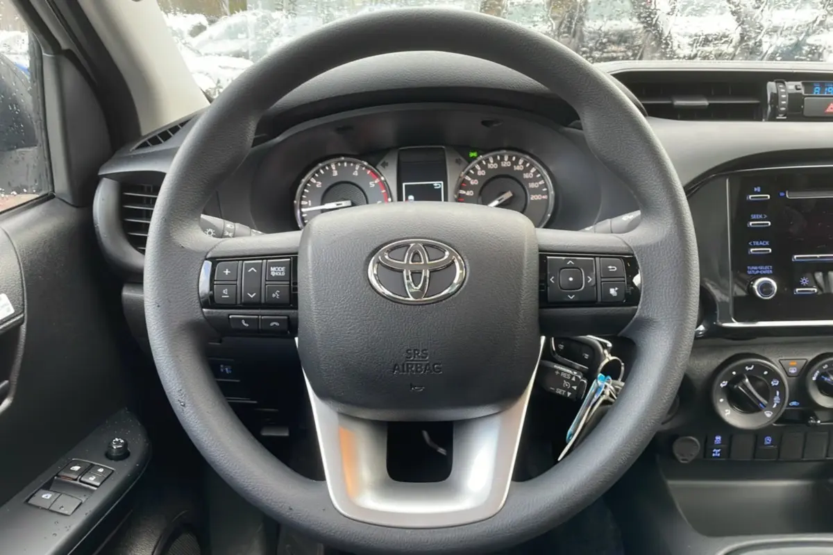Vue rapprochée du volant noir du Toyota Hilux 2024 avec commandes intégrées et tableau de bord visible.