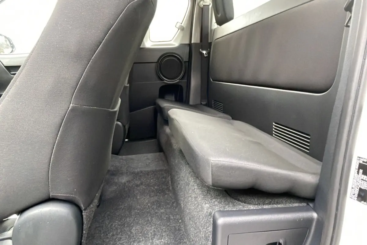 Vue intérieure arrière côté droit du Toyota Hilux 4x4 2024 blanc, montrant la banquette rabattue et les sièges noirs.