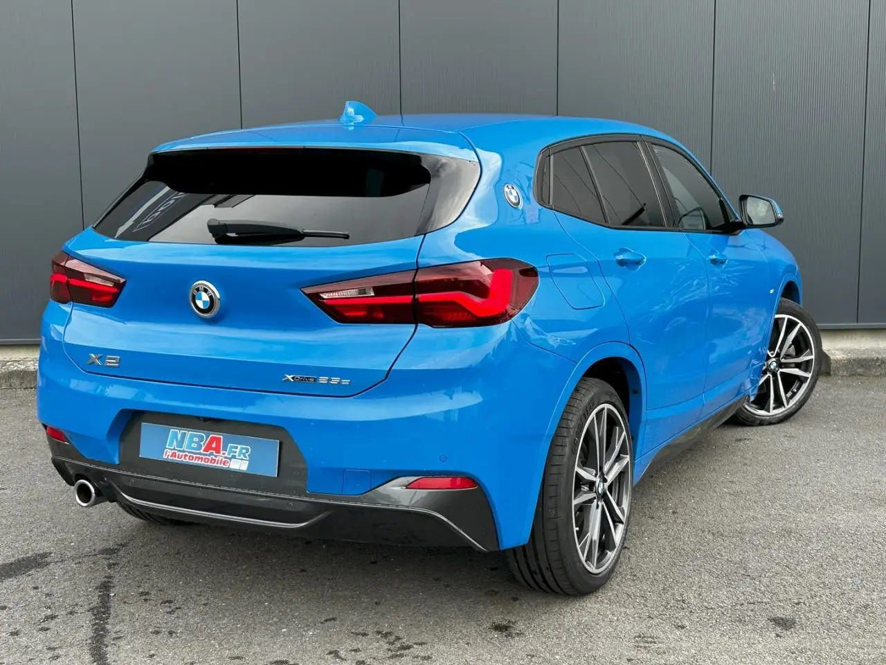 Vue 3/4 arrière droite d'un BMW X2 F39 xDrive 25e bleu Misano avec jantes alliage bicolores et hayon électrique.
