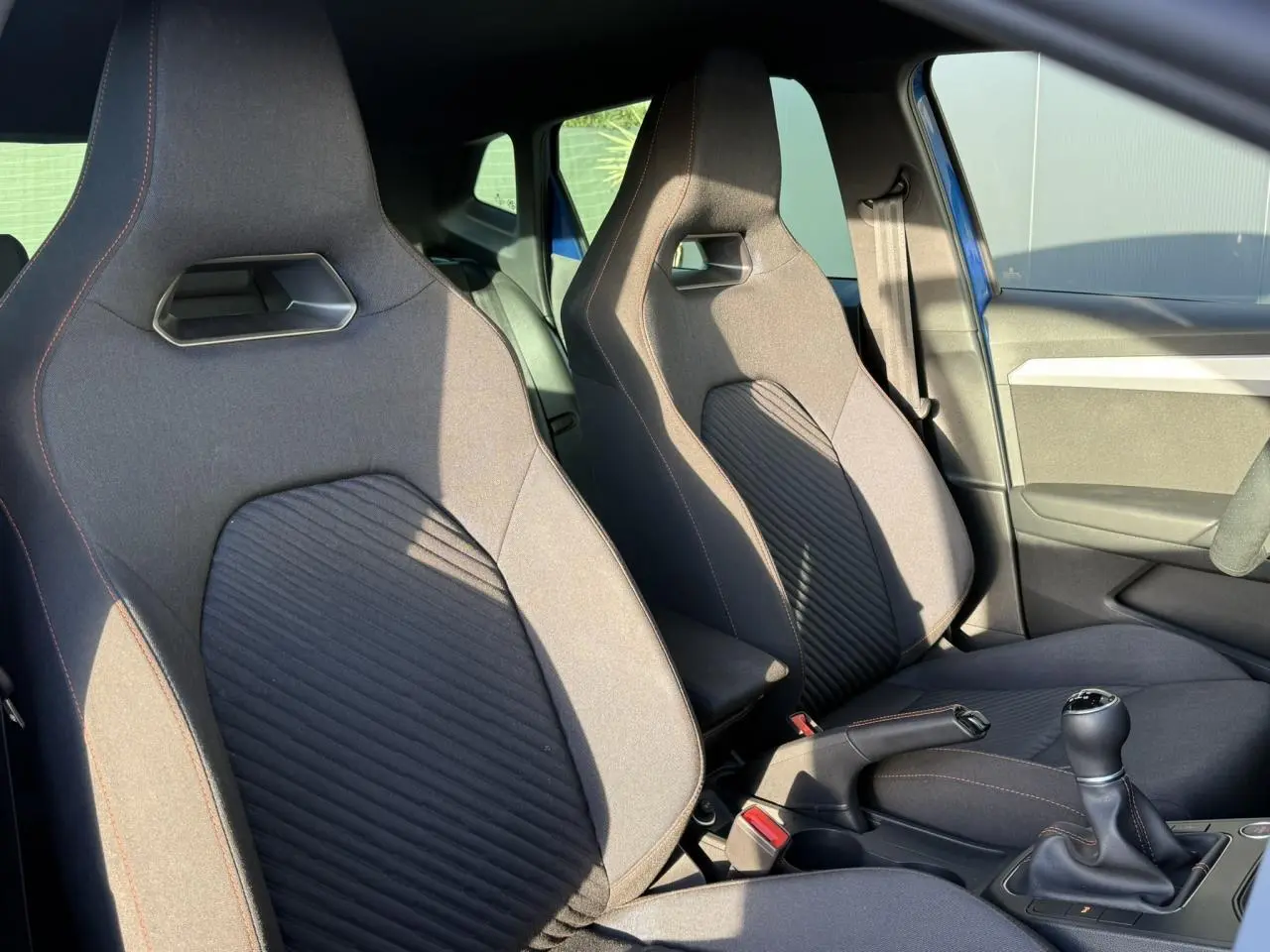 Vue intérieure côté avant droit des sièges sport noirs avec surpiqûres orange et levier de vitesse manuel d'une SEAT IBIZA TSI 115 FR bleu saphir 2025.