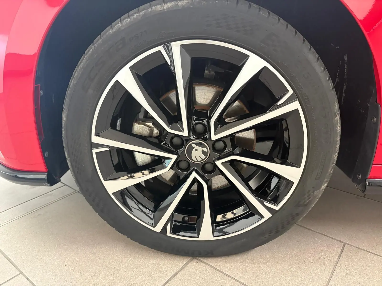 Gros plan sur la jante noire et argentée du côté gauche d'une Skoda Fabia rouge Velvet avec logo au centre.