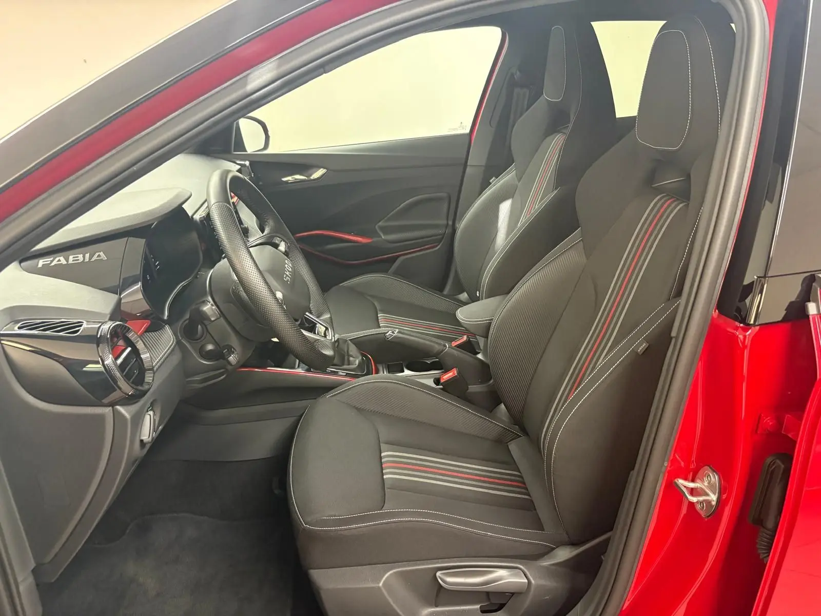 Vue intérieure côté conducteur de la Skoda Fabia rouge velvet avec sièges sport noirs à surpiqûres rouges et toit noir.