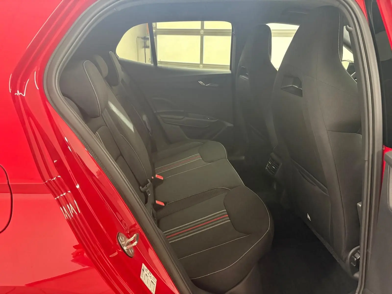 Vue intérieure côté gauche des sièges arrière noirs avec surpiqûres blanches et bandes rouges d'une Skoda Fabia rouge Velvet 2025.